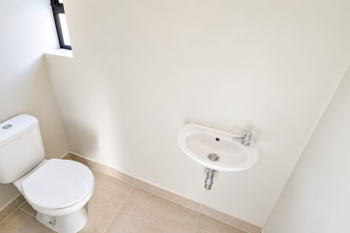 A clean and minimalist guest bathroom featuring a white toilet and a wall-mounted basin with neutral floor tiling.