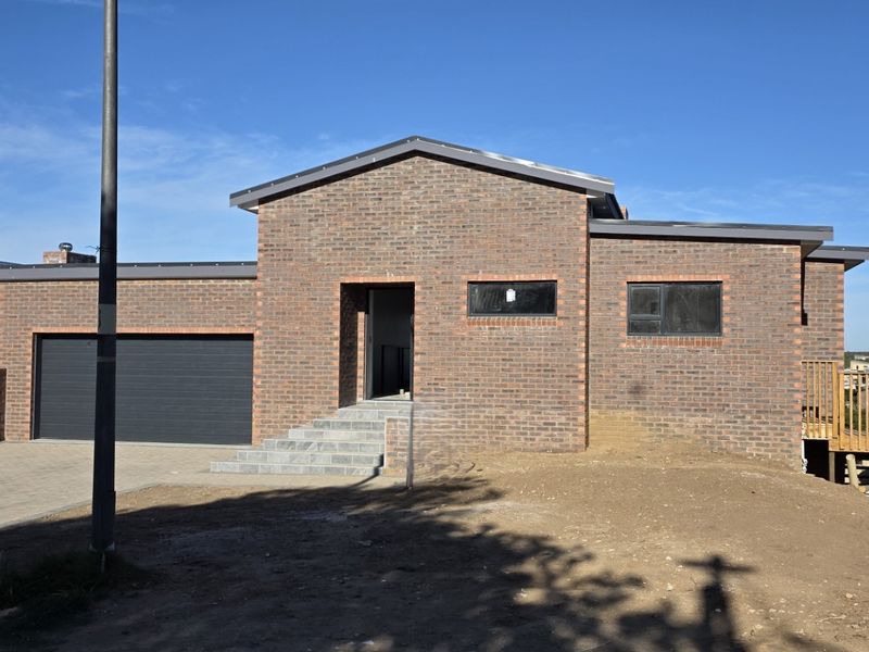 Modern face brick house featuring a double garage, paved driveway, and a timber deck, currently undergoing final exterior landscaping.