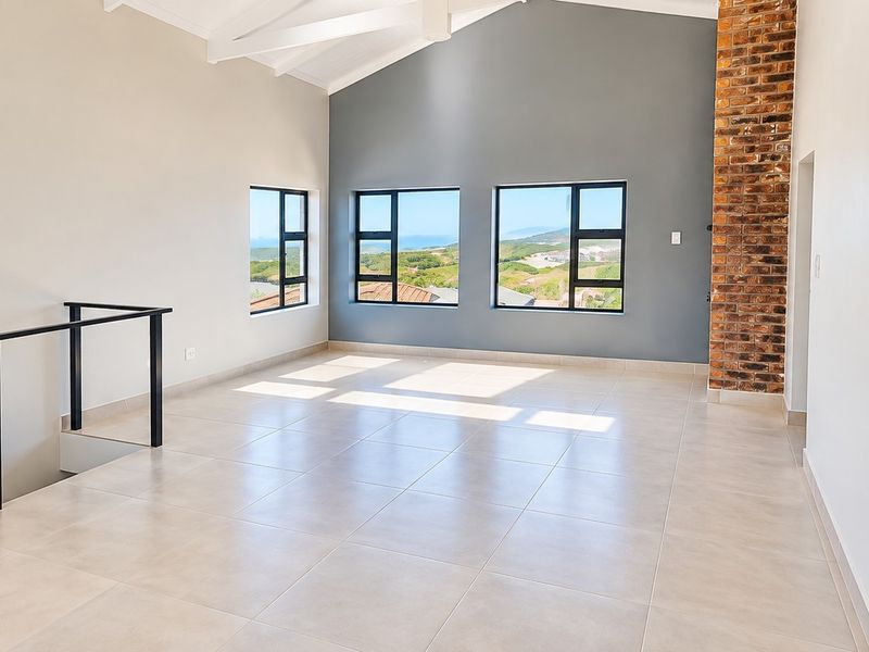 Spacious open-plan living area featuring a vaulted ceiling, tiled floors, and a striking exposed brick chimney breast with scenic views.