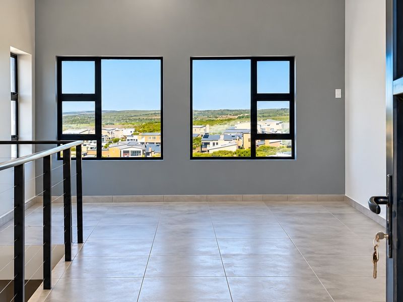 A bright, modern landing or hallway area featuring large windows with scenic views, tiled flooring, and a sleek black metal balustrade.