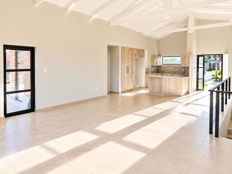 Spacious open-plan living area featuring a vaulted ceiling, exposed brick fireplace, tiled floors, and an integrated kitchen, leading to a staircase.