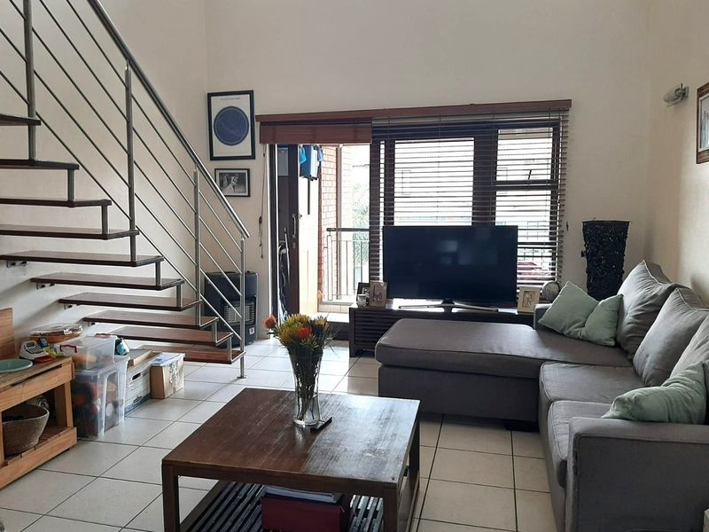 Open-plan living area featuring a modern staircase with stainless steel balustrades, tiled flooring, and direct access to an outdoor balcony.
