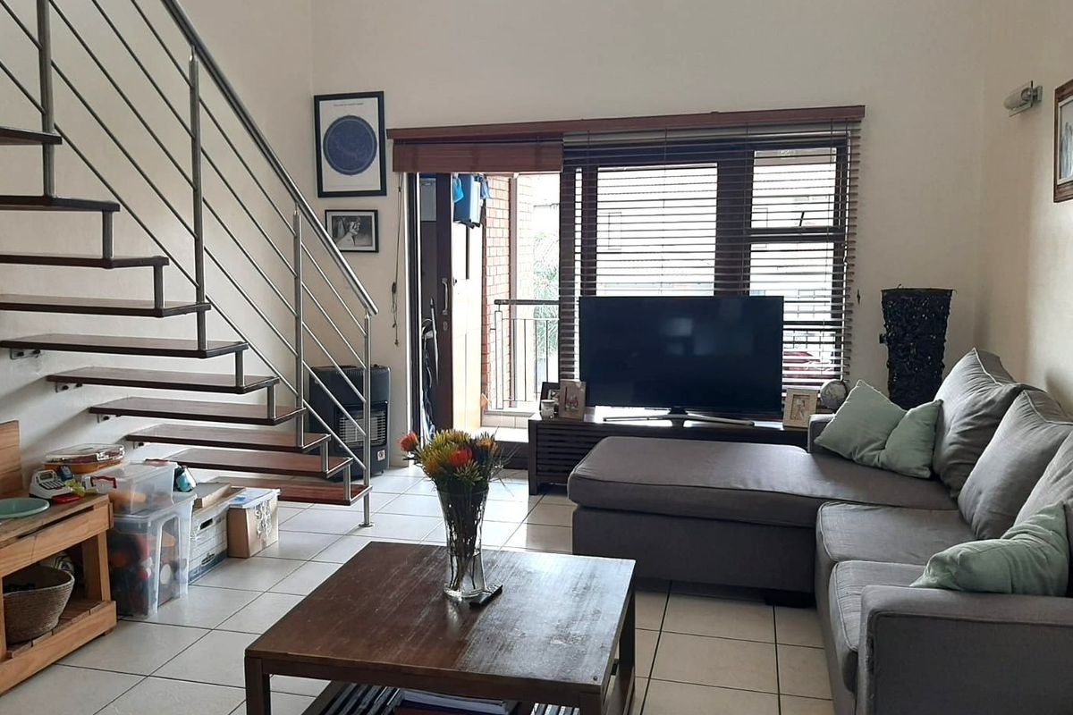 Open-plan living area featuring a modern staircase with stainless steel balustrades, tiled flooring, and direct access to an outdoor balcony.
