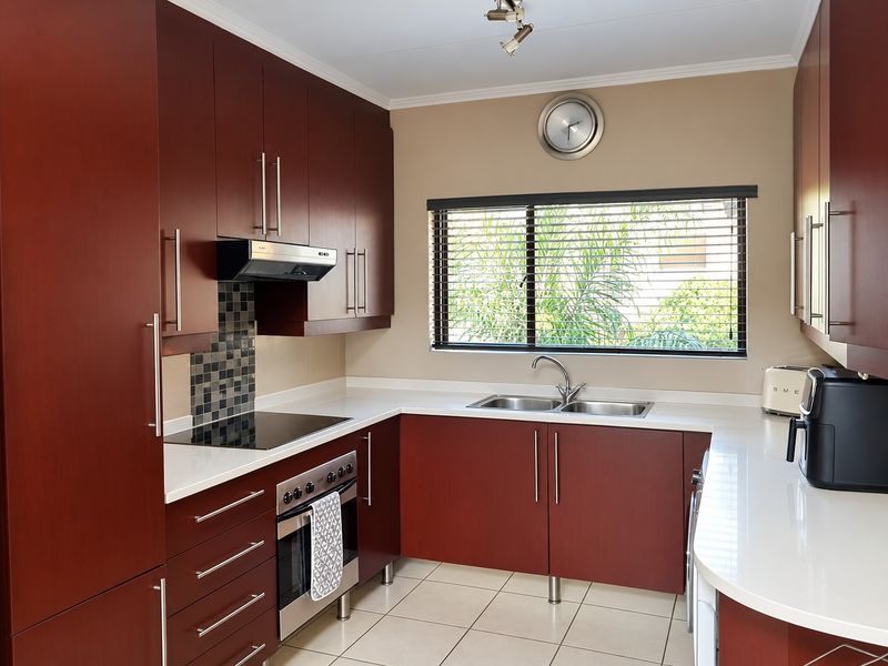 A well-maintained kitchen featuring dark wood cabinetry, stone countertops, integrated appliances, and a tiled backsplash, offering a clean and functional workspace.