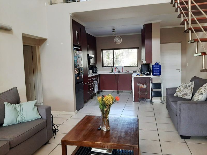 Open-plan living area featuring a kitchen with dark cabinetry, tiled flooring, and a staircase leading to an upper level.