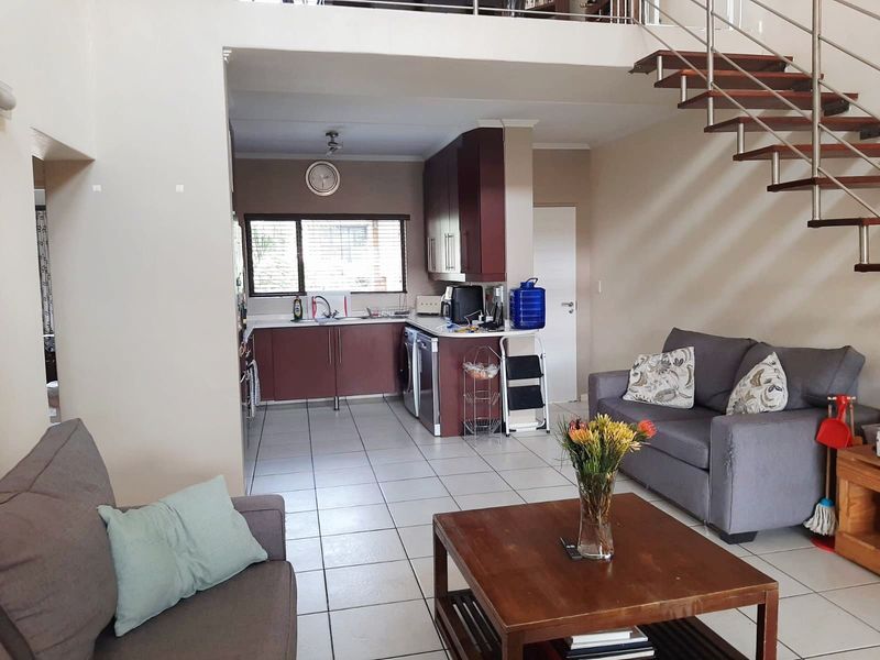 Open-plan living area featuring a kitchen with built-in cabinetry, tiled flooring, and a modern staircase leading to an upper level.