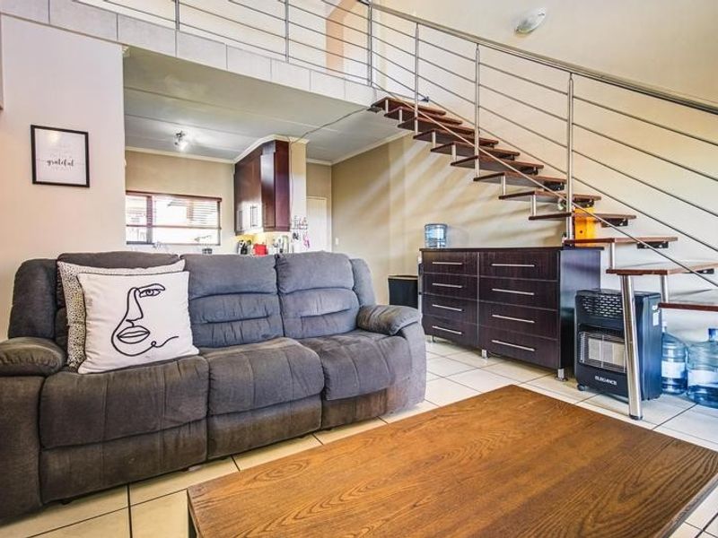 Open plan living area featuring a modern staircase with stainless steel balustrade, tiled flooring, and a view through to the kitchen area.
