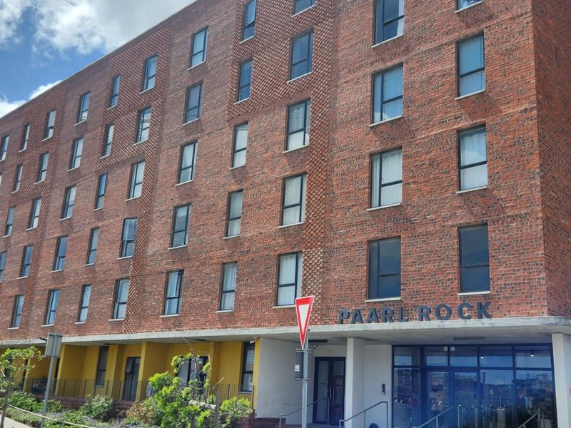 A multi-story apartment building featuring a classic red brick facade, large windows, and a prominent concrete entrance overhang.