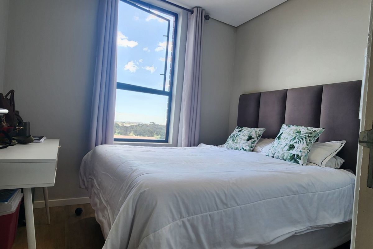 A well-lit bedroom featuring laminate flooring and a large window with natural light, providing a comfortable and inviting living space.