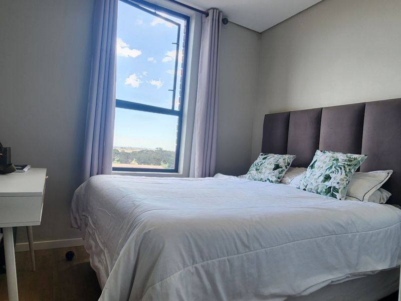 A well-lit bedroom featuring laminate flooring and a large window with natural light, providing a comfortable and inviting living space.