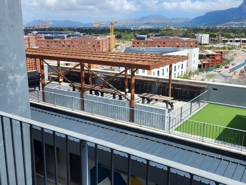 A rooftop terrace featuring a timber pergola, metal balustrades, and artificial grass, offering expansive urban and mountain views.