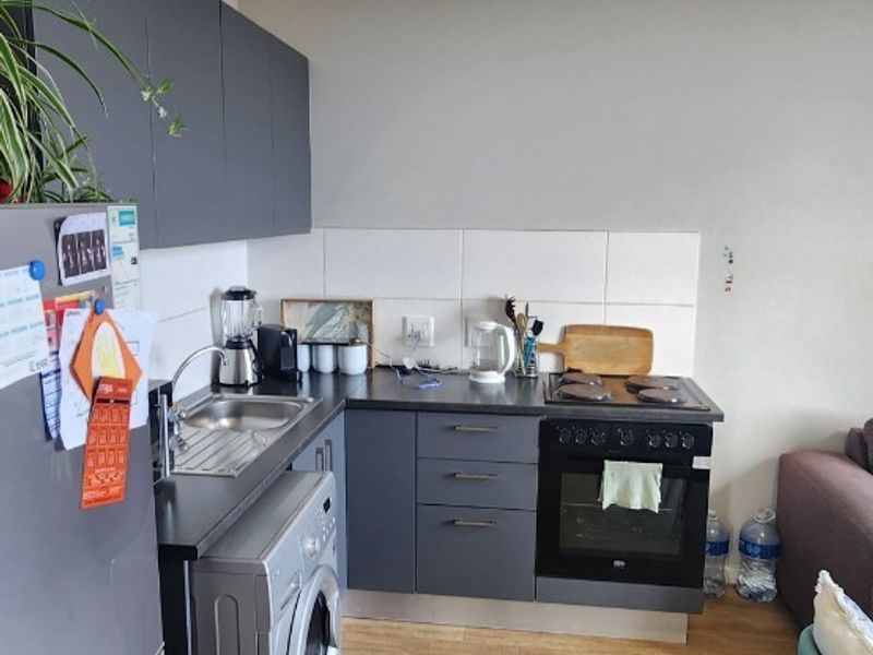 A compact, modern kitchen featuring dark grey cabinetry, laminate countertops, a built-in oven with hob, and a tiled splashback, integrated into an open-plan living space.