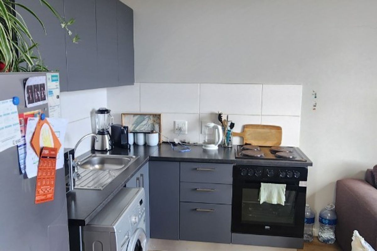 A compact, modern kitchen featuring dark grey cabinetry, laminate countertops, a built-in oven with hob, and a tiled splashback, integrated into an open-plan living space.