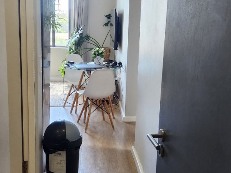 A view from the apartment entrance looking down the hallway towards the living area, featuring laminate flooring and natural light from a large window.