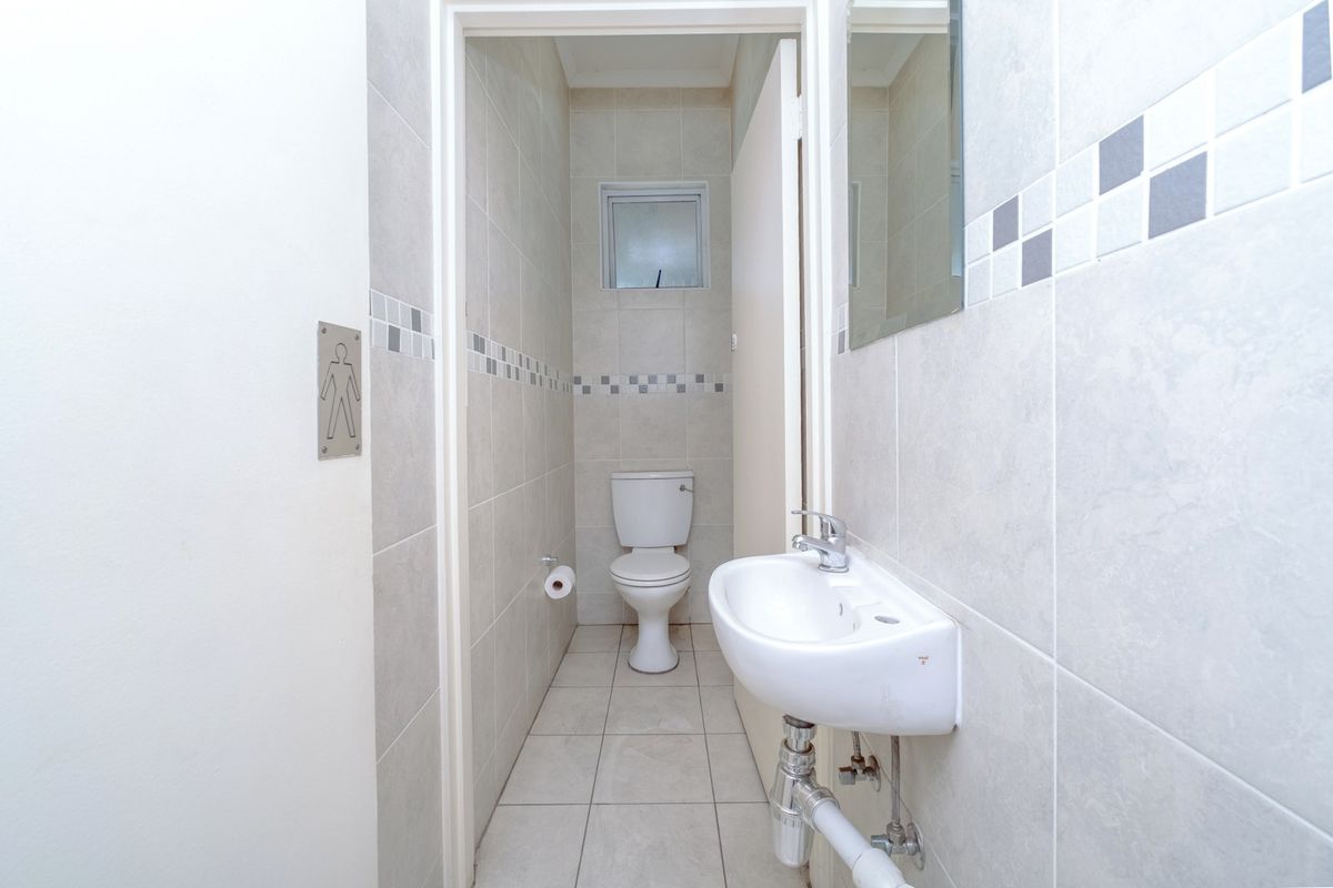 A clean and functional office restroom featuring a wall-mounted basin, toilet, and neutral ceramic tiling throughout.