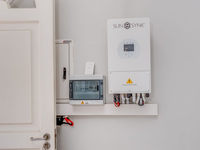 A clean utility area featuring a wall-mounted Sunsynk solar inverter and associated electrical distribution board.