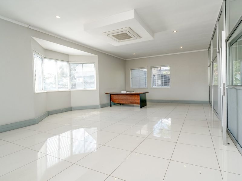 A bright, spacious office featuring polished tile flooring, recessed lighting, ducted air conditioning, and large windows with venetian blinds, enclosed by a glass partition.
