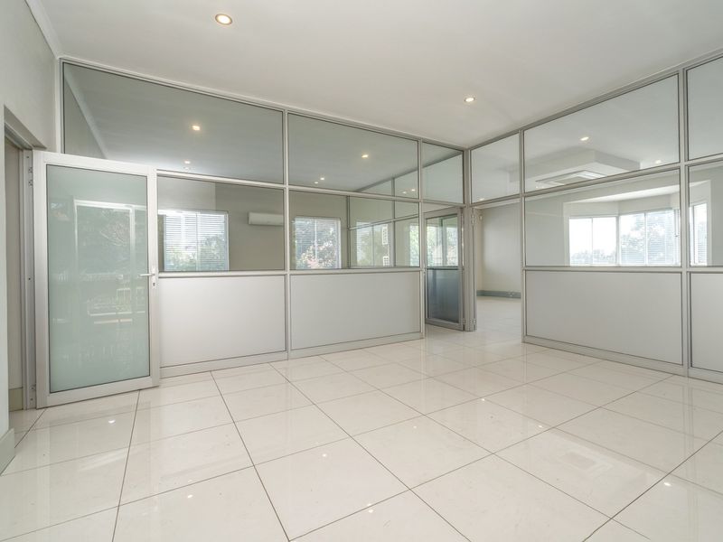 A bright, modern office space featuring glass partition walls, tiled flooring, and recessed lighting, offering a clean and professional environment.