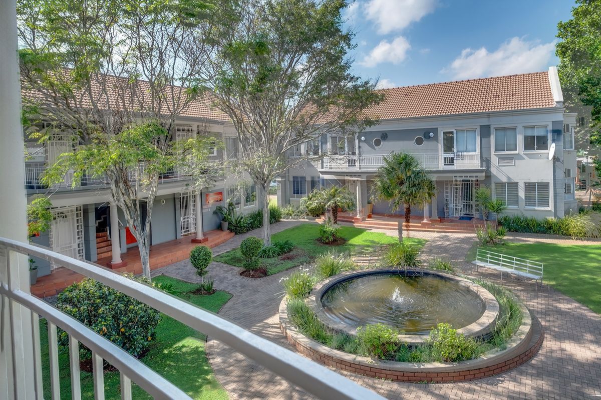 A well-maintained office complex courtyard featuring a central water fountain, paved walkways, landscaped gardens, and multi-level building access with balconies.