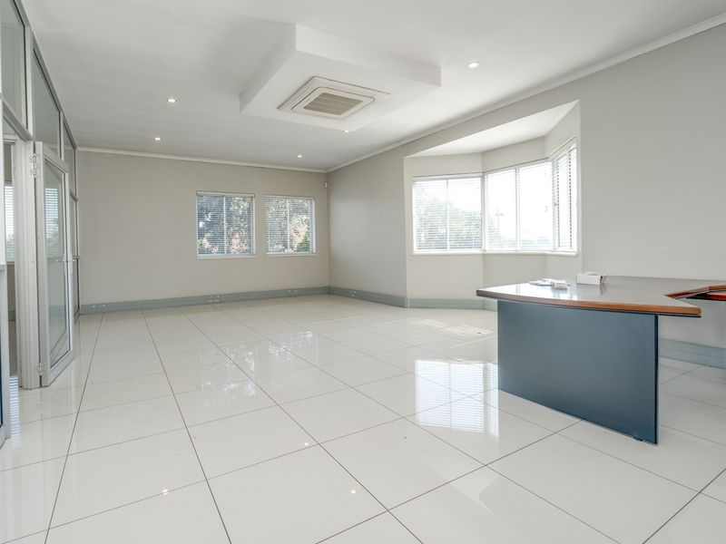 A bright and spacious open-plan office area featuring polished tiled floors, recessed ceiling lighting, integrated air conditioning, and large windows with aluminium frames.
