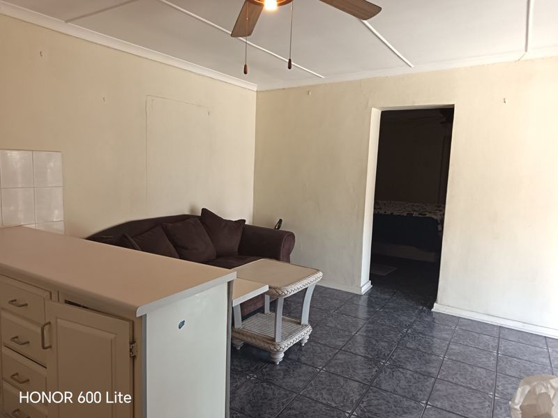 Open plan living area featuring tiled flooring, a ceiling fan, and kitchen cabinetry, showing signs of wear and requiring cosmetic updates.