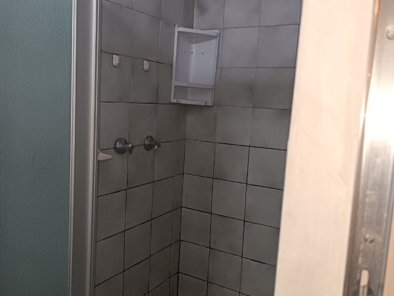 A dated shower stall featuring tiled walls and flooring, currently showing significant wear and requiring renovation to improve its condition and aesthetic appeal.