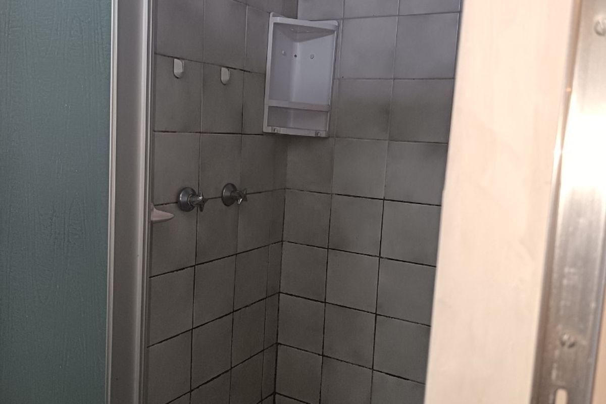 A dated shower stall featuring tiled walls and flooring, currently showing significant wear and requiring renovation to improve its condition and aesthetic appeal.