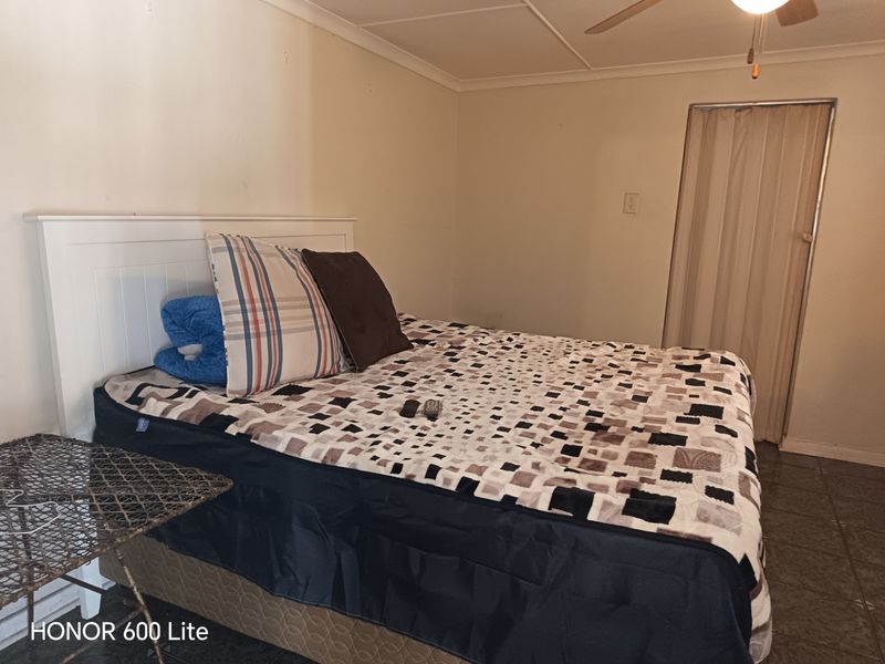 A bedroom featuring tiled flooring, a ceiling fan, and a folding door, currently showing signs of wear and dated finishes.