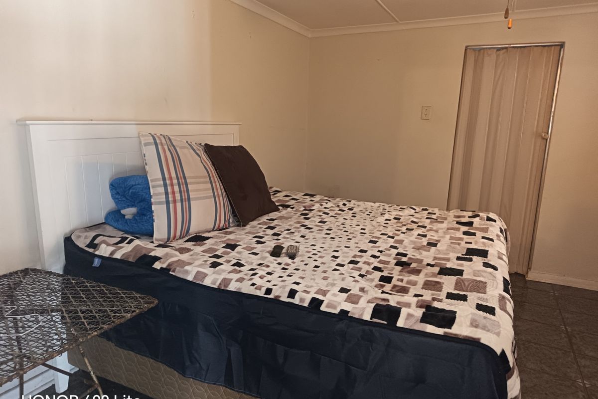 A bedroom featuring tiled flooring, a ceiling fan, and a folding door, currently showing signs of wear and dated finishes.