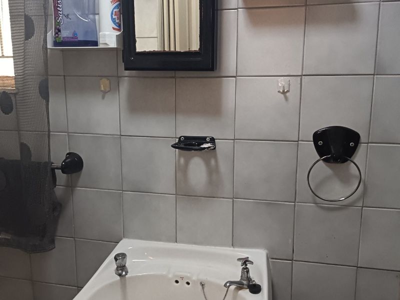 A functional bathroom featuring a wall-mounted basin with dual taps, tiled wall finishes, and integrated bathroom accessories.