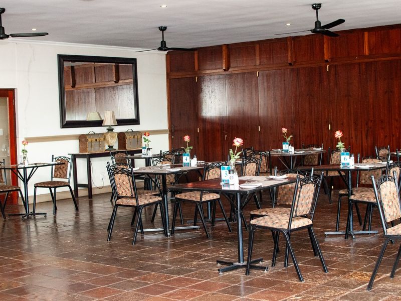 A spacious dining area featuring dark wood wall paneling, tiled flooring, and ceiling fans, suitable for a restaurant or communal dining space.