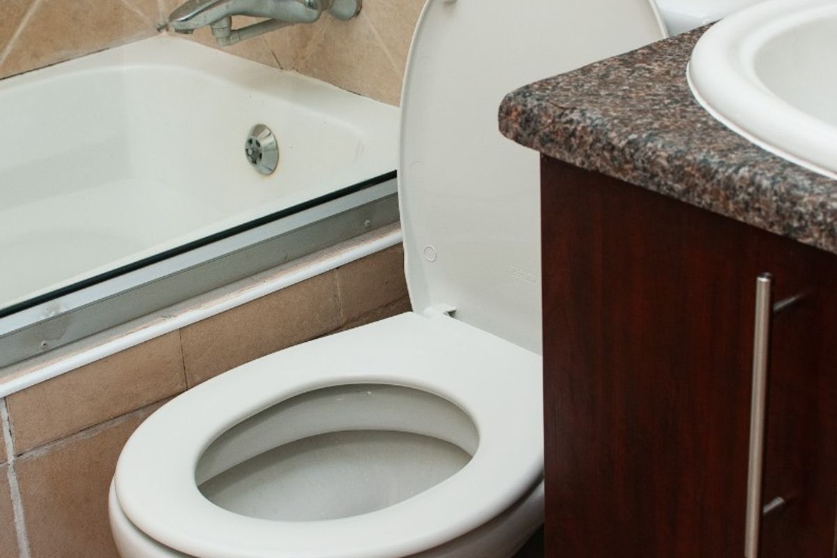 A functional bathroom featuring a bathtub with shower mixer, a standard toilet, and a vanity cabinet with a granite countertop and drop-in sink.