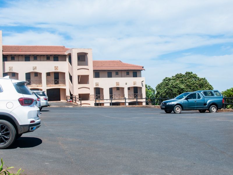 Exterior view of an apartment complex featuring a paved parking area and multi-level building facade with terracotta roofing.