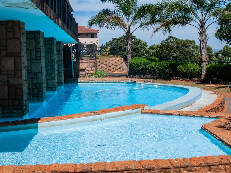 Outdoor swimming pool area featuring stone-clad pillars, a tiered pool design, and landscaped garden surroundings.