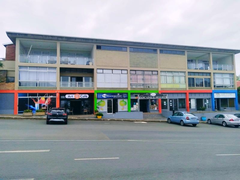 A multi-level commercial building facade featuring various storefronts on the ground floor and residential balconies on the upper levels.
