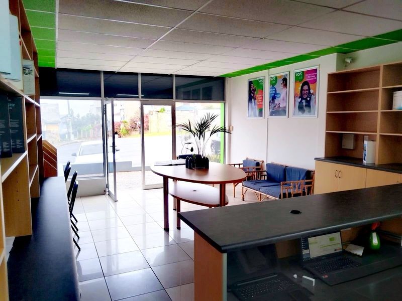 A bright retail entry space featuring tiled flooring, a suspended ceiling, built-in shelving units, and a functional reception counter with glass storefront access.