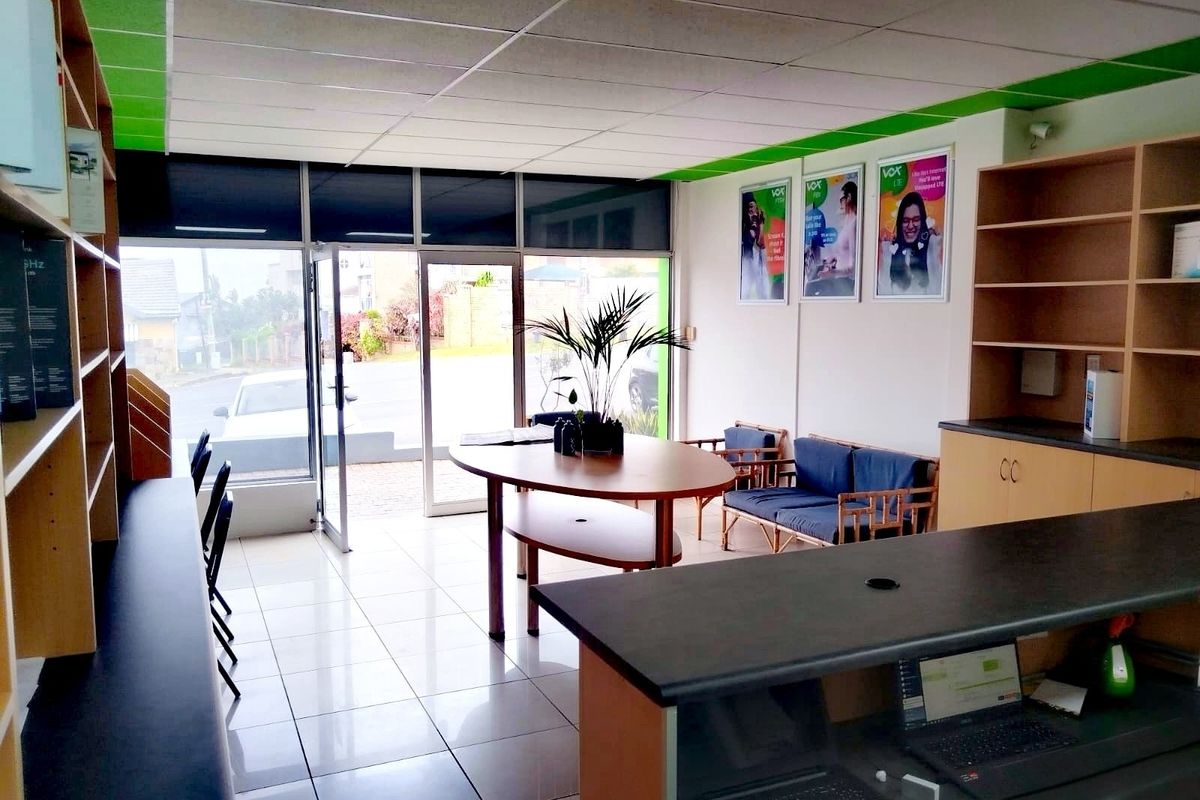 A bright retail entry space featuring tiled flooring, a suspended ceiling, built-in shelving units, and a functional reception counter with glass storefront access.