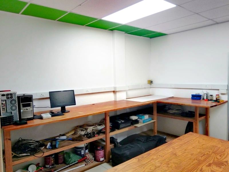 A functional utility or workshop space featuring a large built-in wooden workbench, suspended ceiling with integrated lighting, and perimeter electrical trunking.