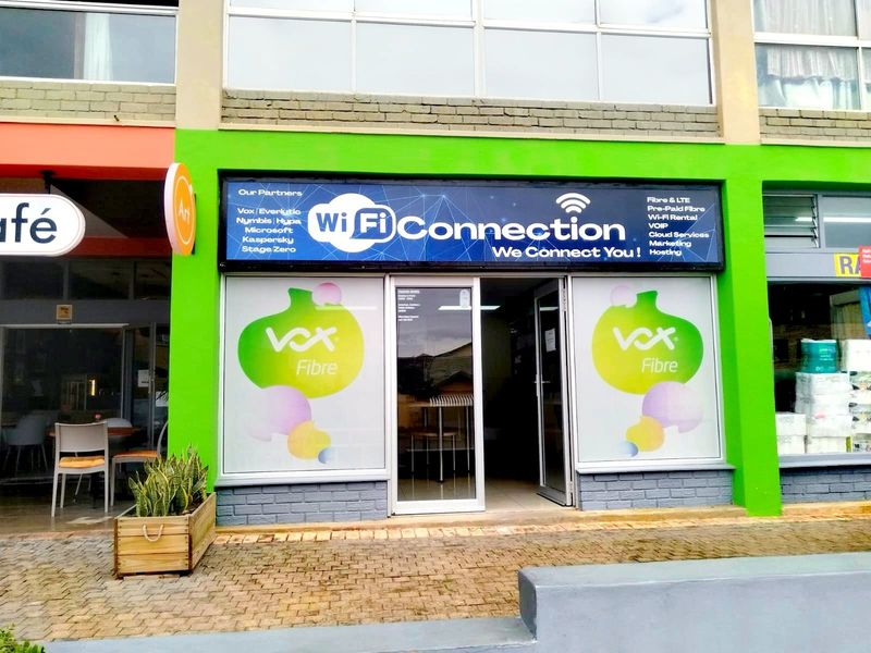 Front facade of a retail unit featuring a glass storefront, prominent signage, and paved access area.