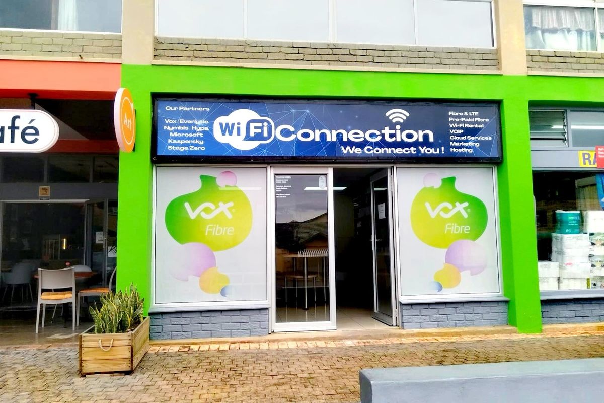 Front facade of a retail unit featuring a glass storefront, prominent signage, and paved access area.