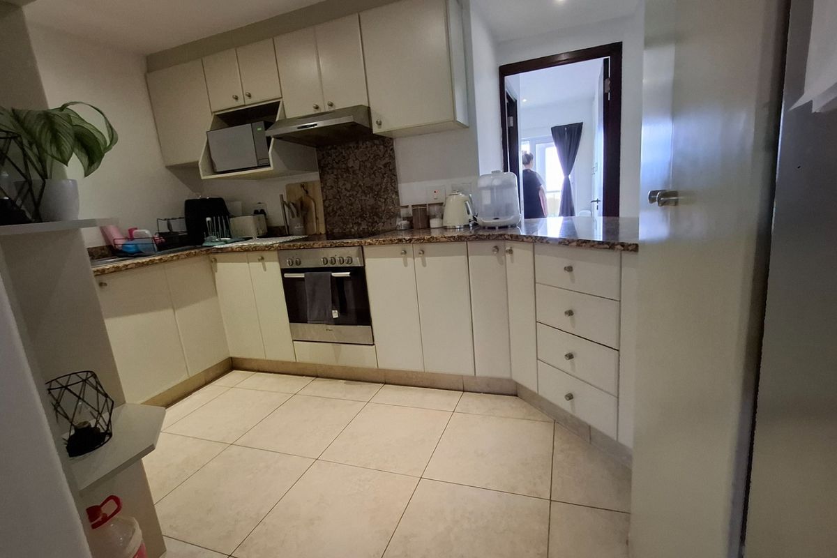 A functional kitchen featuring light-toned cabinetry, granite countertops, built-in oven, and extractor fan, with tiled flooring throughout.