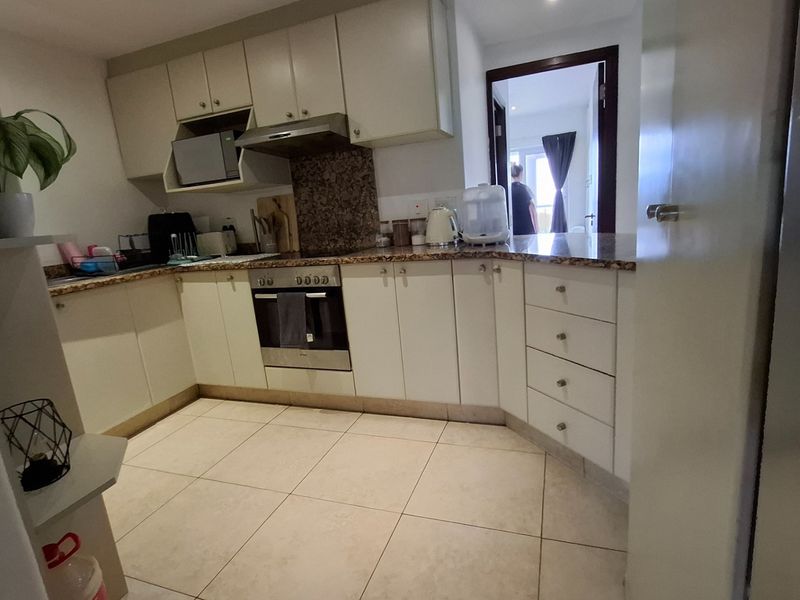 A functional kitchen featuring light-toned cabinetry, granite countertops, built-in oven, and extractor fan, with tiled flooring throughout.