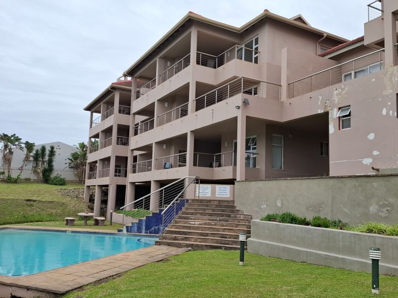 Exterior view of an apartment complex featuring a swimming pool, landscaped lawn, and multi-level balconies with stainless steel railings.