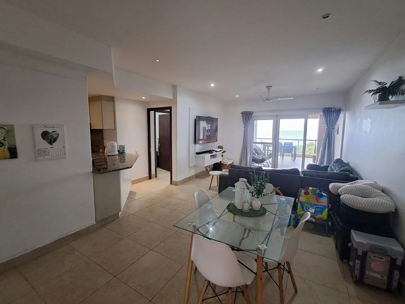 Open-plan living and dining area featuring tiled floors, recessed lighting, and direct access to a balcony with ocean views.