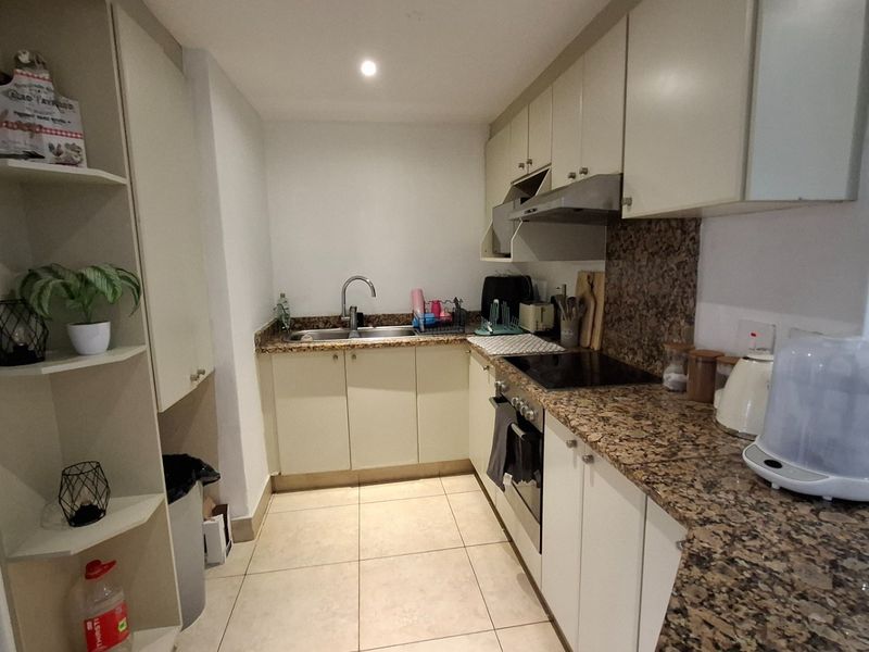 A functional kitchen featuring granite countertops, built-in cabinetry, a stainless steel sink, and integrated appliances including an oven and hob.