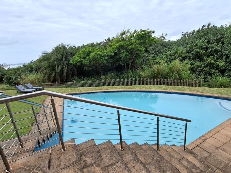 Outdoor swimming pool area featuring stone stairs with a modern stainless steel balustrade, surrounded by a landscaped garden and timber fencing.