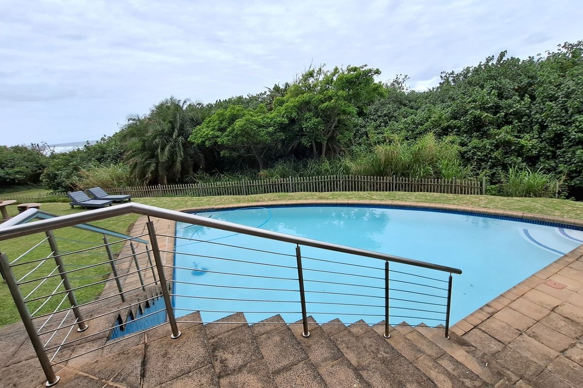 Outdoor swimming pool area featuring stone stairs with a modern stainless steel balustrade, surrounded by a landscaped garden and timber fencing.