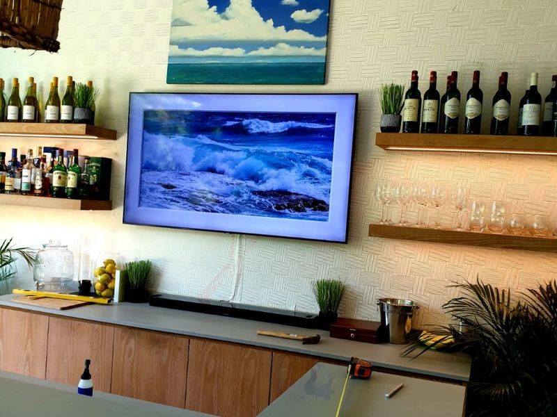 A modern home bar area featuring custom wooden cabinetry, stone countertops, floating shelves with integrated lighting, and decorative textured wallpaper.