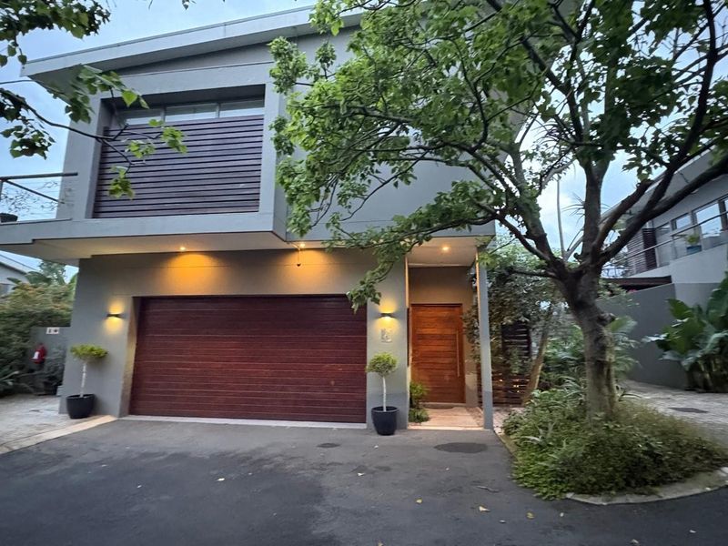 Modern double-storey townhouse facade featuring a timber garage door, matching front entrance, and contemporary architectural lighting.
