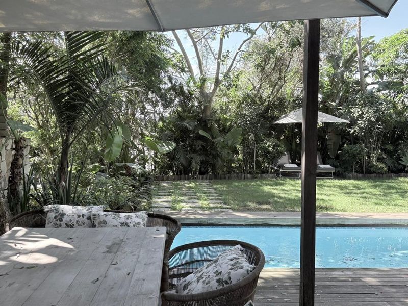 Covered outdoor patio area featuring timber decking overlooking a private swimming pool and lush garden setting.